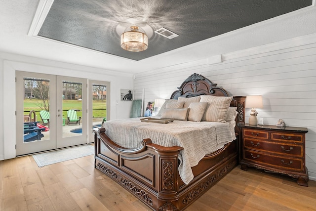 bedroom with access to exterior, french doors, a textured ceiling, and light wood finished floors