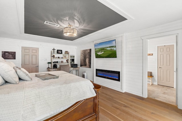 bedroom featuring visible vents, a raised ceiling, wood finished floors, and a glass covered fireplace