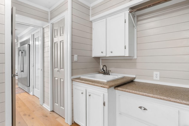 kitchen with light wood-style floors, white cabinetry, a sink, wood walls, and stainless steel built in refrigerator