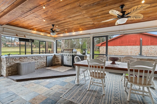 unfurnished sunroom featuring a ceiling fan, wood ceiling, and a healthy amount of sunlight