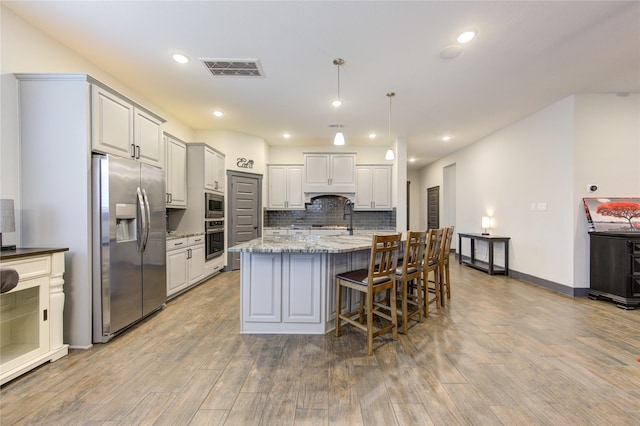 kitchen with a center island with sink, visible vents, appliances with stainless steel finishes, hanging light fixtures, and light stone countertops