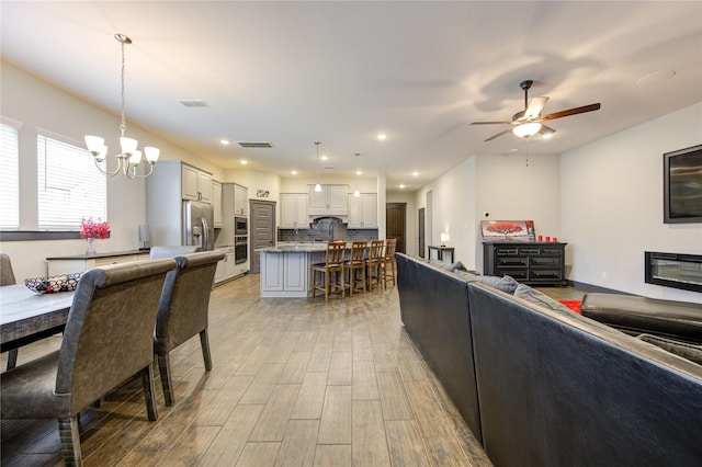 interior space featuring light wood-style floors, recessed lighting, visible vents, and ceiling fan with notable chandelier