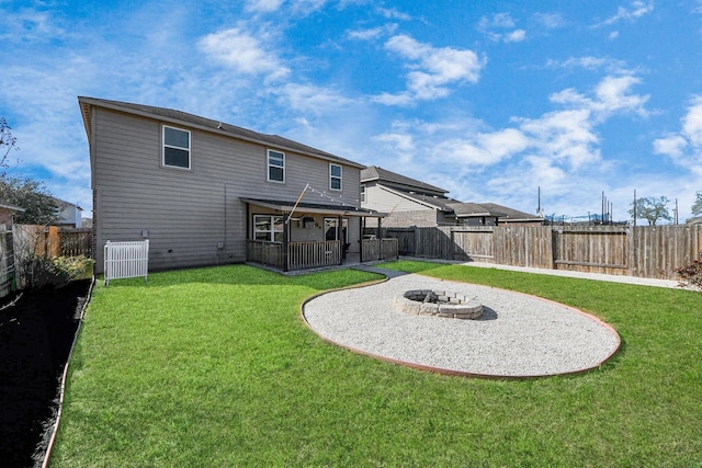 rear view of house with a fenced backyard, a fire pit, and a lawn