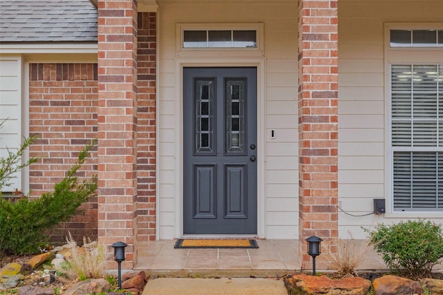 doorway to property with brick siding and roof with shingles