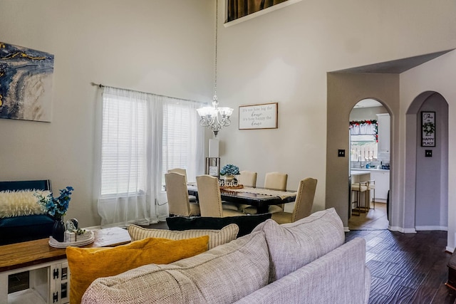 living area featuring baseboards, arched walkways, a towering ceiling, dark wood-type flooring, and an inviting chandelier