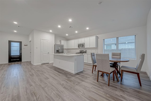 kitchen with white cabinets, appliances with stainless steel finishes, a kitchen island with sink, light countertops, and light wood-type flooring