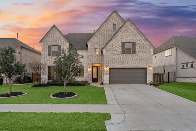 french provincial home with driveway, a yard, fence, and brick siding