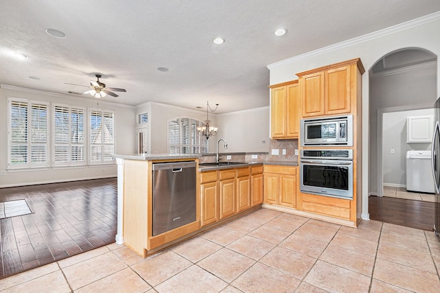 kitchen with crown molding, light tile patterned floors, appliances with stainless steel finishes, a sink, and a peninsula