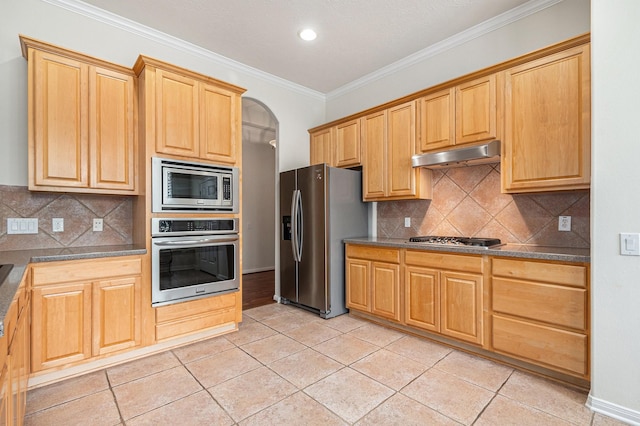 kitchen featuring dark countertops, ornamental molding, stainless steel appliances, under cabinet range hood, and light tile patterned flooring