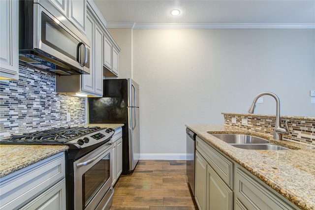 kitchen with light stone counters, dark wood finished floors, stainless steel appliances, ornamental molding, and a sink