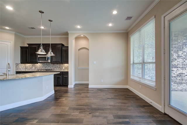 kitchen featuring visible vents, arched walkways, stainless steel microwave, hanging light fixtures, and a sink