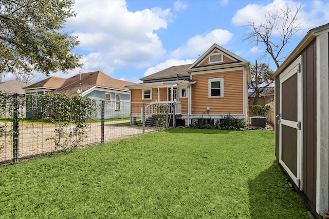 rear view of property with central air condition unit, fence, and a yard