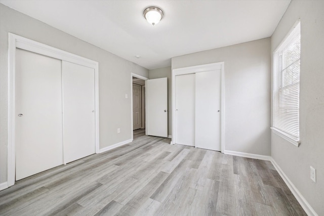 unfurnished bedroom featuring light wood-type flooring, two closets, and baseboards