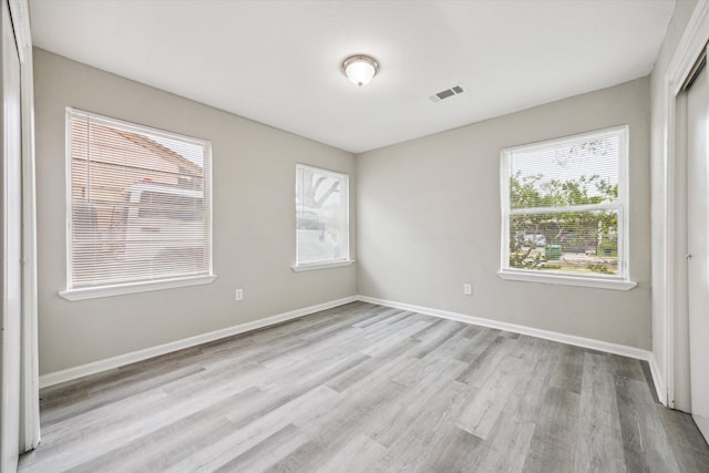 empty room with light wood-type flooring, visible vents, and baseboards