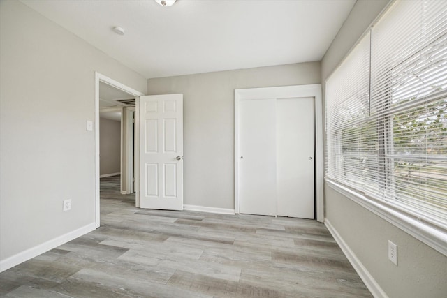 unfurnished bedroom with a closet, light wood-style flooring, and baseboards