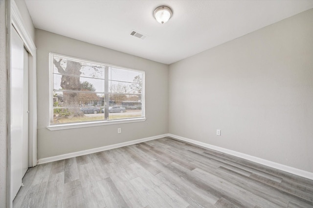 empty room featuring light wood-type flooring, visible vents, and baseboards