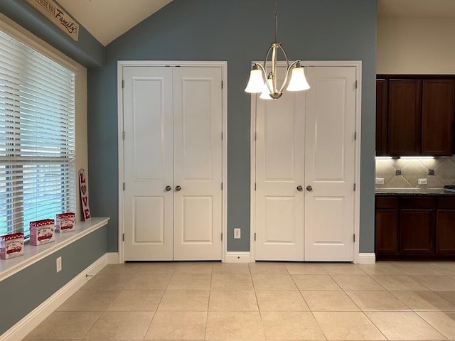 unfurnished dining area featuring lofted ceiling, light tile patterned floors, baseboards, and a chandelier