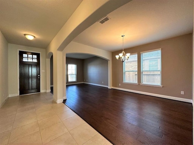 entryway with wood finished floors, visible vents, baseboards, an inviting chandelier, and arched walkways