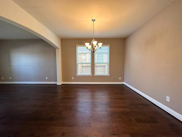 empty room featuring a chandelier, dark wood finished floors, arched walkways, and baseboards