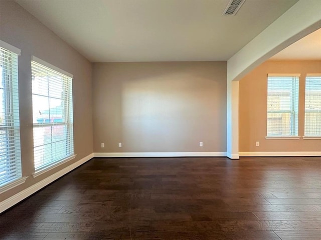 unfurnished room featuring visible vents, baseboards, and dark wood-style floors