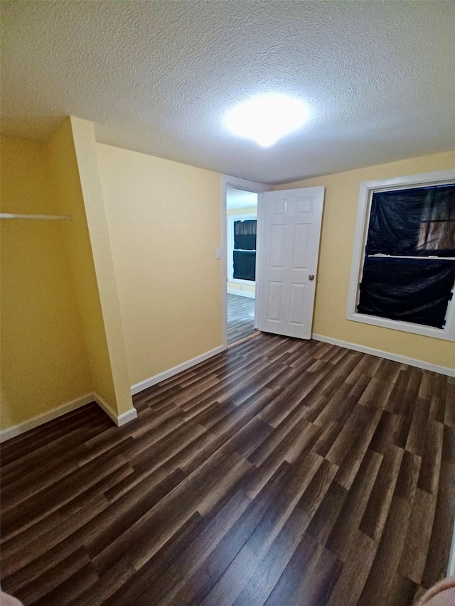 spare room featuring a textured ceiling, dark wood finished floors, and baseboards