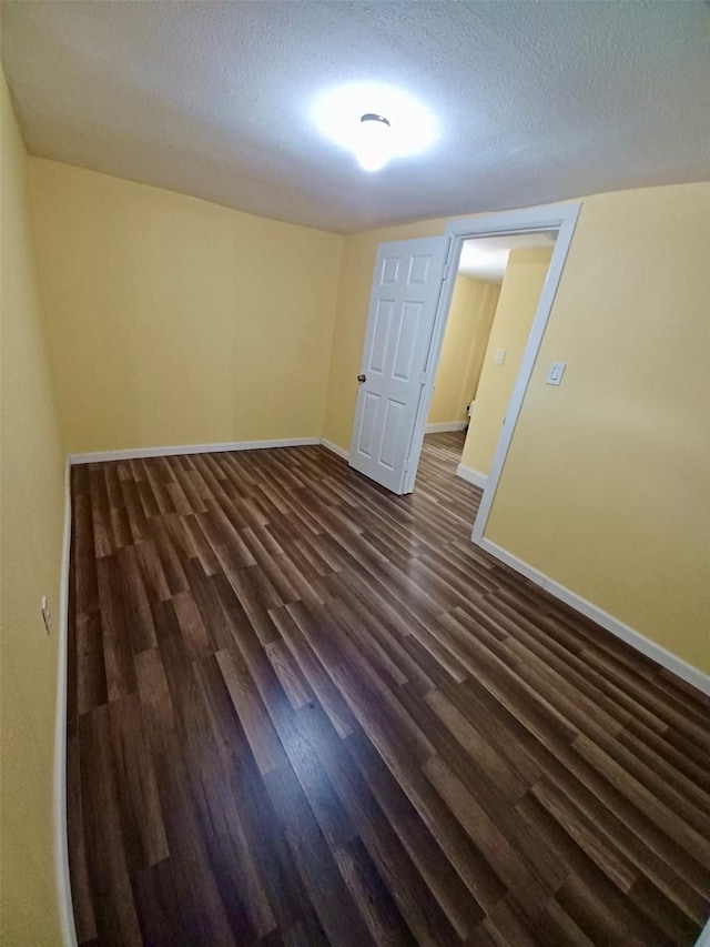 empty room with dark wood-type flooring, a textured ceiling, and baseboards