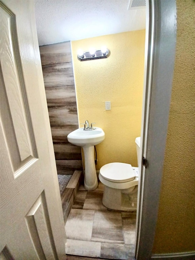 half bath featuring a sink, a textured wall, visible vents, and toilet