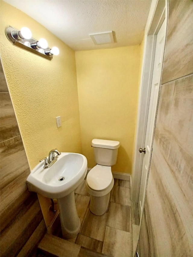 bathroom with a textured wall, toilet, a sink, a textured ceiling, and wood finished floors