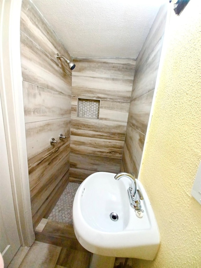 bathroom featuring wooden walls, tiled shower, a textured wall, a textured ceiling, and a sink