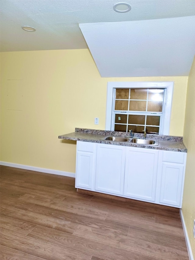 kitchen with baseboards, lofted ceiling, light wood-type flooring, white cabinetry, and a sink