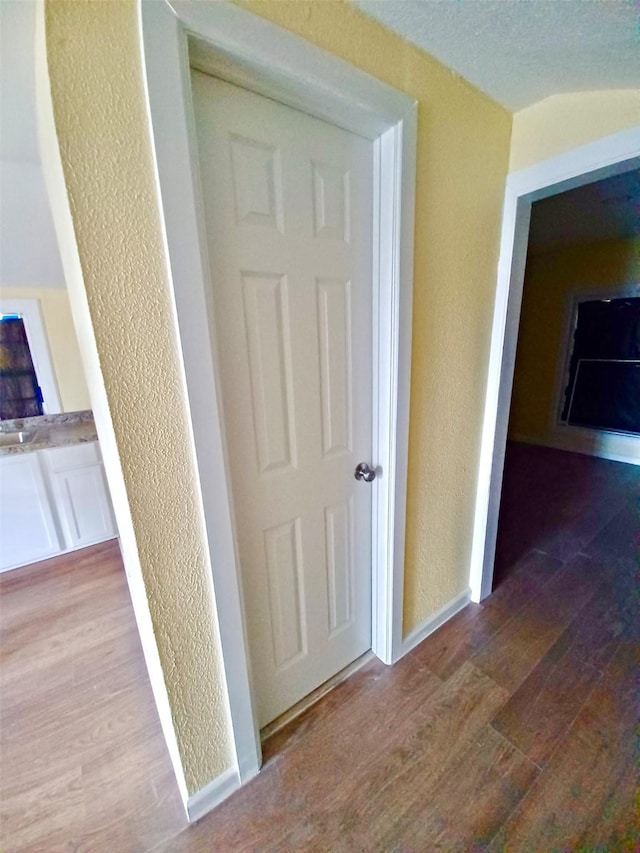 corridor featuring a textured wall, wood finished floors, and baseboards