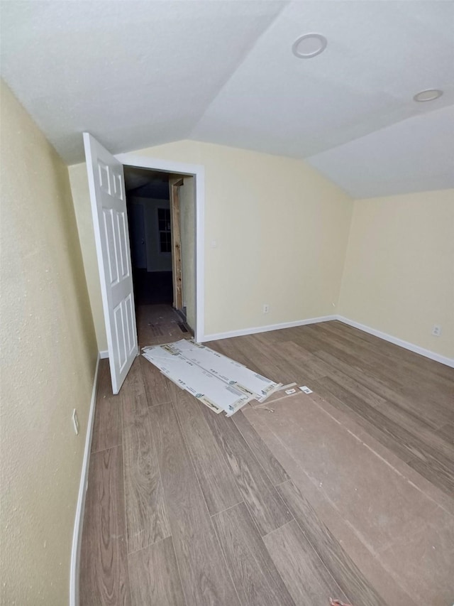 interior space featuring vaulted ceiling, wood finished floors, and baseboards