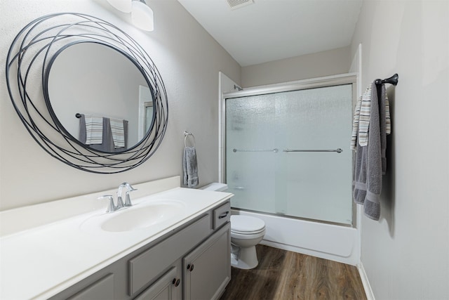 full bath with toilet, bath / shower combo with glass door, wood finished floors, and vanity