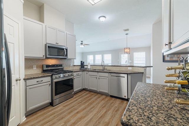 kitchen with tasteful backsplash, appliances with stainless steel finishes, light wood-type flooring, pendant lighting, and a sink