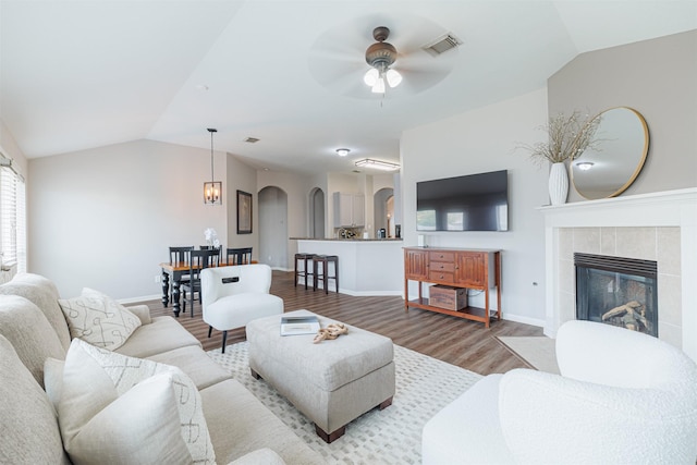 living room with lofted ceiling, visible vents, arched walkways, and wood finished floors