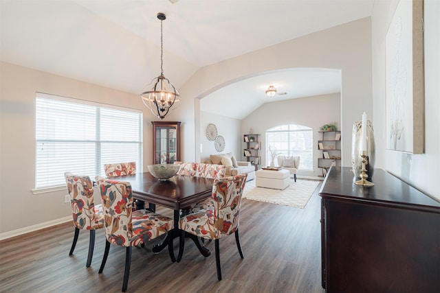 dining room featuring lofted ceiling, arched walkways, a chandelier, dark wood-type flooring, and baseboards