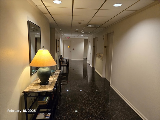 corridor with a paneled ceiling, granite finish floor, and baseboards