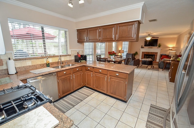 kitchen featuring appliances with stainless steel finishes, brown cabinetry, open floor plan, a sink, and a peninsula