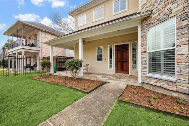 entrance to property featuring fence, stucco siding, a yard, stone siding, and a ceiling fan