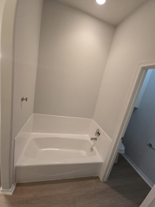 full bath with wood finished floors, a bath, and baseboards