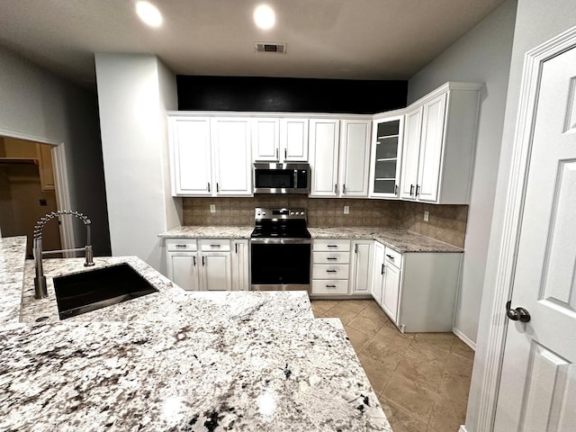 kitchen featuring visible vents, glass insert cabinets, appliances with stainless steel finishes, white cabinetry, and a sink