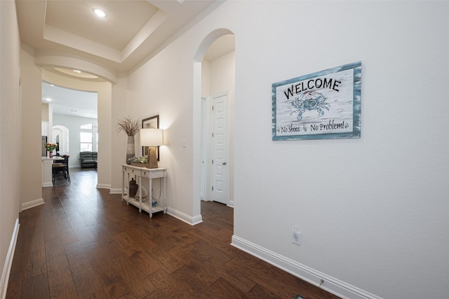 corridor featuring dark wood-style floors, baseboards, and arched walkways