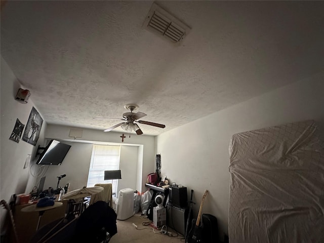 carpeted home office featuring a ceiling fan, visible vents, and a textured ceiling