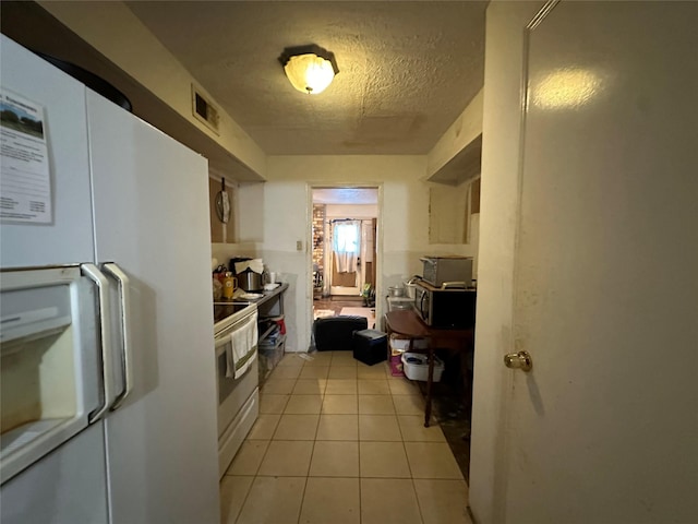 kitchen with light tile patterned floors, a textured ceiling, white appliances, visible vents, and white cabinets