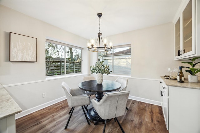 dining space with dark wood-type flooring, a chandelier, and baseboards