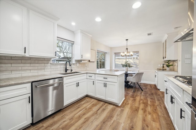 kitchen with stainless steel appliances, white cabinets, a sink, wall chimney range hood, and a peninsula