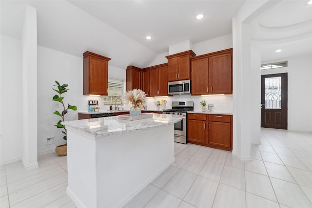 kitchen with light stone counters, stainless steel appliances, a kitchen island, brown cabinets, and decorative backsplash