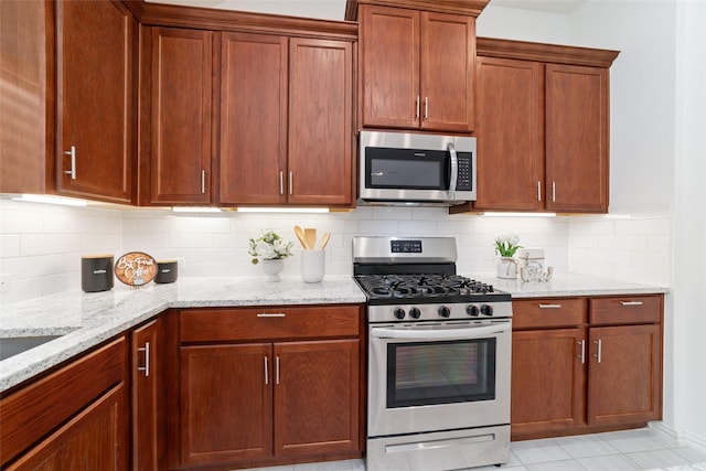 kitchen with stainless steel appliances, light tile patterned flooring, backsplash, and light stone countertops