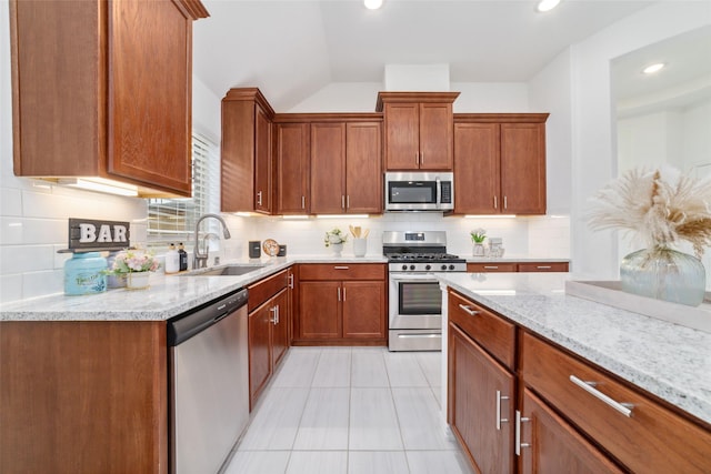 kitchen with appliances with stainless steel finishes, a sink, and light stone counters