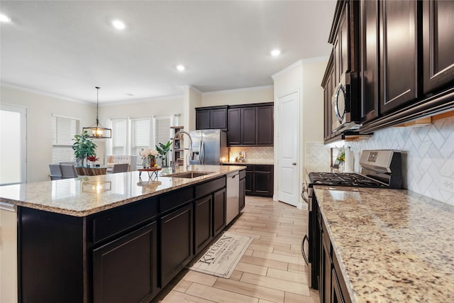 kitchen featuring a center island with sink, stainless steel appliances, hanging light fixtures, a sink, and light stone countertops